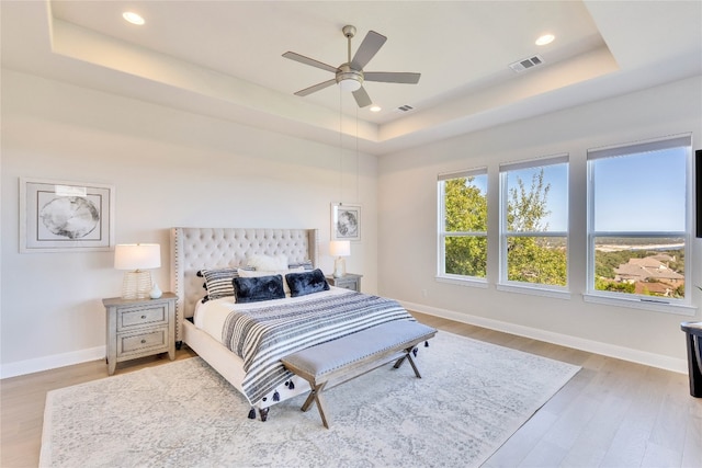 bedroom with ceiling fan, a raised ceiling, and light hardwood / wood-style flooring