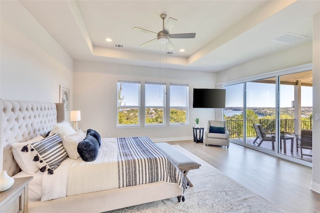 bedroom with access to exterior, wood-type flooring, a raised ceiling, and ceiling fan