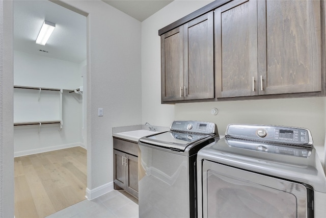 laundry area with washer and clothes dryer, cabinets, sink, and light hardwood / wood-style flooring