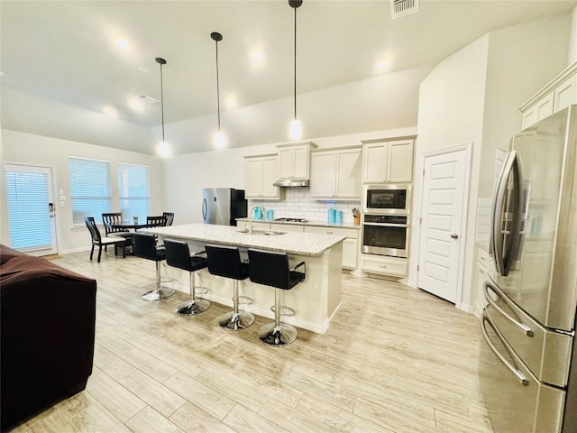 kitchen featuring appliances with stainless steel finishes, a center island with sink, white cabinets, light hardwood / wood-style floors, and hanging light fixtures