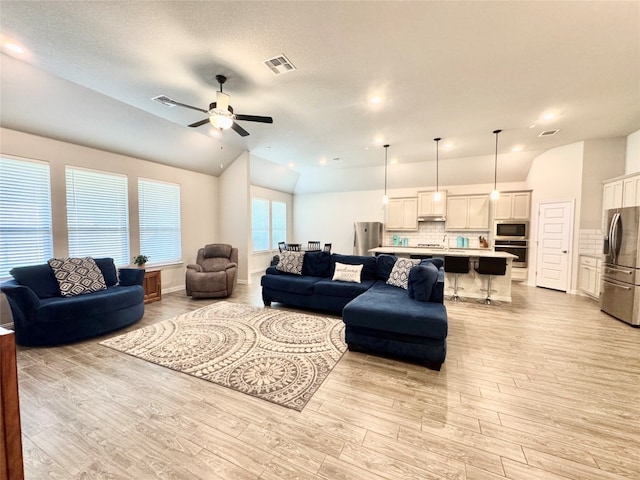 living room featuring a textured ceiling, light hardwood / wood-style flooring, vaulted ceiling, and ceiling fan