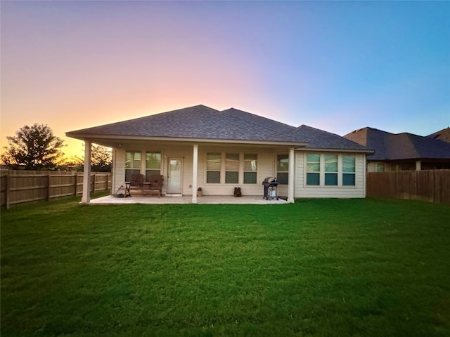 back house at dusk with a lawn and a patio