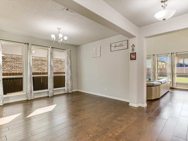 empty room featuring a chandelier, a textured ceiling, and dark wood-type flooring