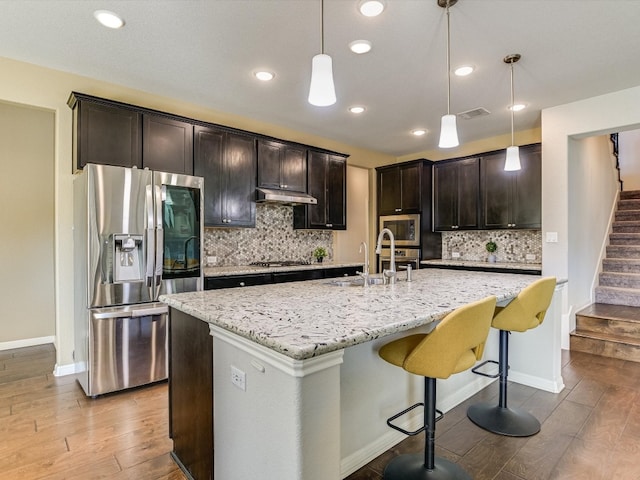 kitchen featuring sink, an island with sink, light hardwood / wood-style floors, pendant lighting, and appliances with stainless steel finishes