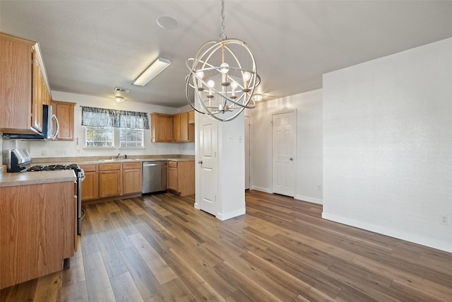 kitchen with appliances with stainless steel finishes, dark hardwood / wood-style floors, decorative light fixtures, a notable chandelier, and sink