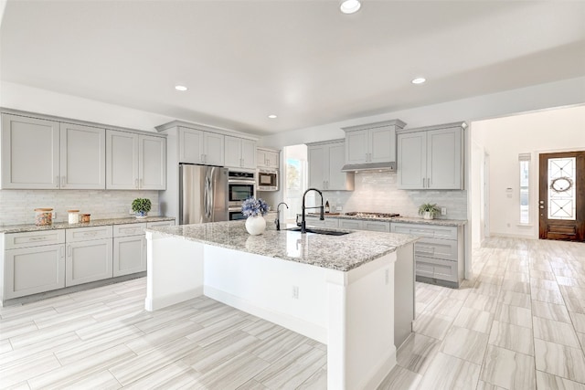 kitchen with sink, stainless steel appliances, light stone counters, gray cabinets, and a kitchen island with sink