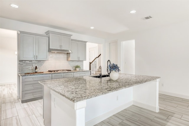 kitchen featuring a large island with sink, light stone counters, gray cabinetry, and sink