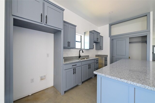 kitchen featuring tasteful backsplash, gray cabinets, light stone counters, and sink