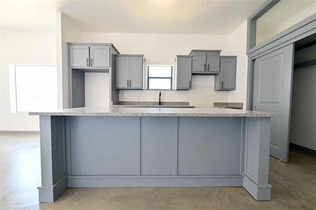 kitchen with gray cabinetry, decorative backsplash, a center island, and light stone counters