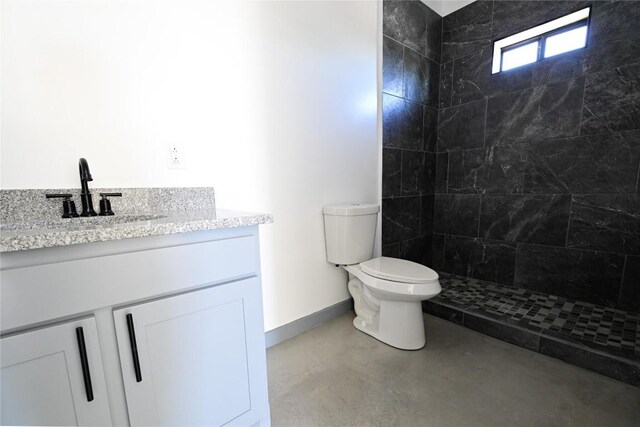 bathroom with a tile shower, vanity, concrete flooring, and toilet