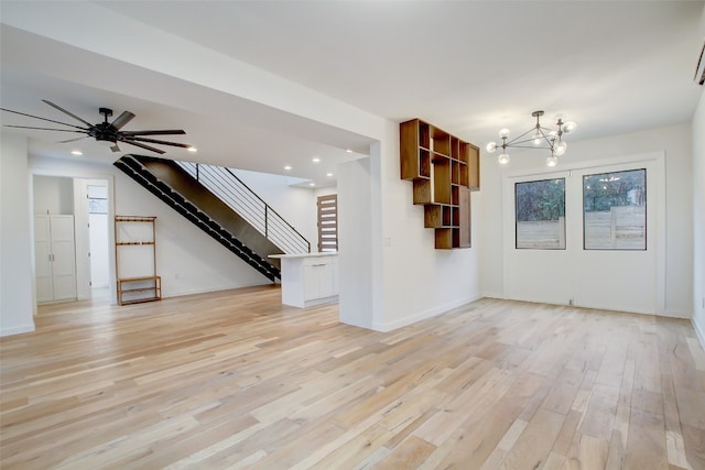 unfurnished living room featuring ceiling fan with notable chandelier and light hardwood / wood-style flooring