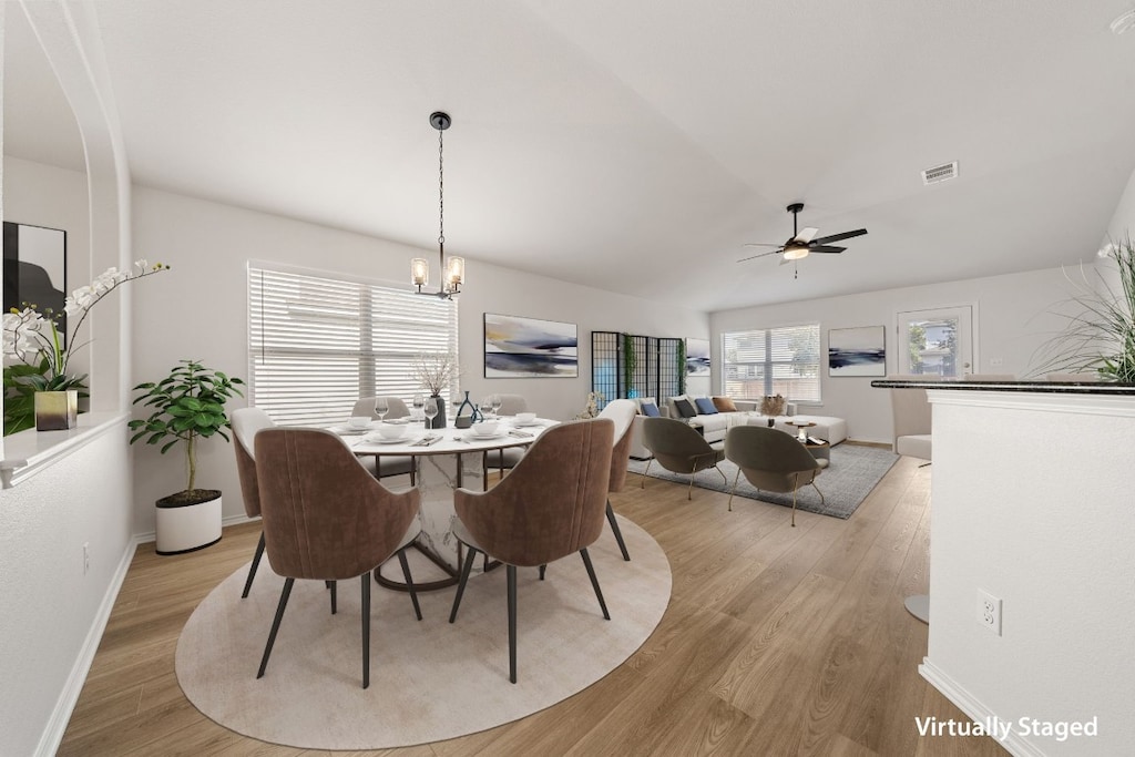 dining room featuring ceiling fan with notable chandelier, light hardwood / wood-style floors, and lofted ceiling