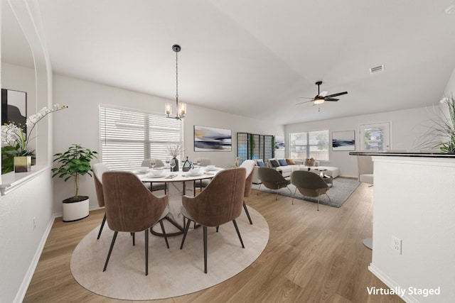 dining room featuring ceiling fan with notable chandelier, light hardwood / wood-style floors, and lofted ceiling