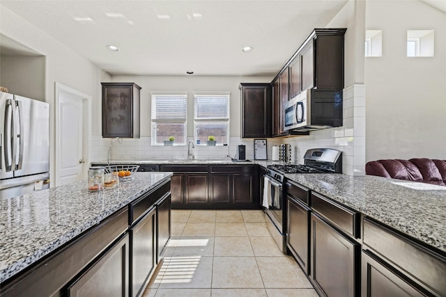 kitchen with light stone countertops, stainless steel appliances, decorative backsplash, dark brown cabinets, and light tile patterned floors