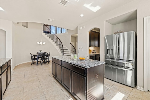 kitchen featuring light stone countertops, dark brown cabinetry, stainless steel refrigerator with ice dispenser, and a kitchen island with sink