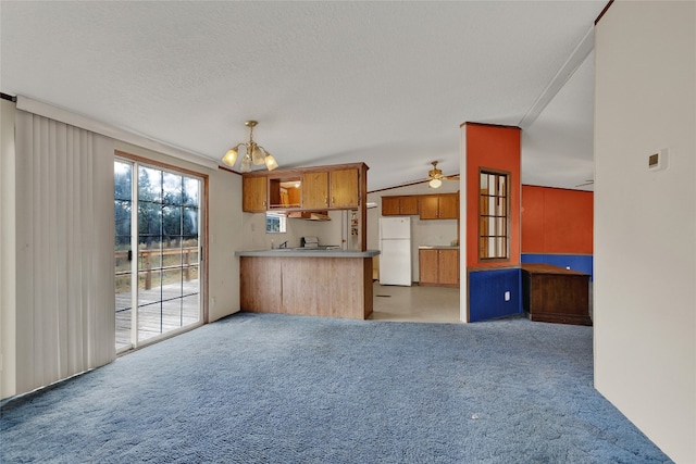 kitchen with kitchen peninsula, a textured ceiling, vaulted ceiling, white refrigerator, and hanging light fixtures