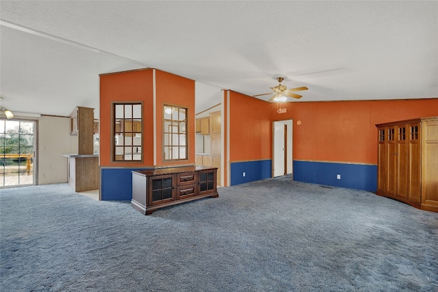 unfurnished living room featuring lofted ceiling, ceiling fan, carpet floors, and a textured ceiling