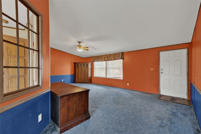 unfurnished living room with dark colored carpet, a textured ceiling, vaulted ceiling, and ceiling fan