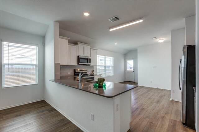 kitchen featuring white cabinets, sink, vaulted ceiling, kitchen peninsula, and stainless steel appliances