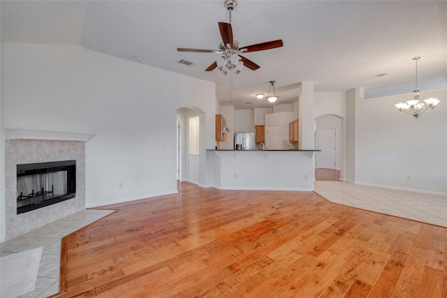 unfurnished living room featuring arched walkways, ceiling fan with notable chandelier, a fireplace, and light wood-style floors