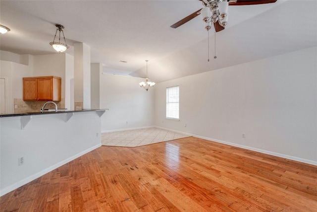 unfurnished living room featuring vaulted ceiling, ceiling fan with notable chandelier, light wood-type flooring, and baseboards