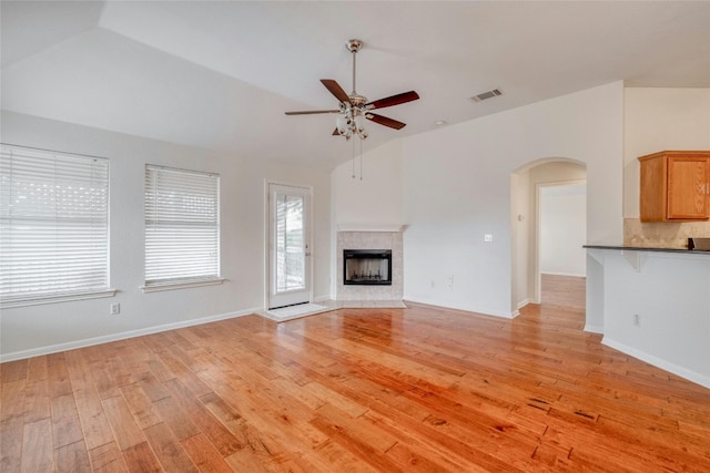 unfurnished living room featuring light wood finished floors, arched walkways, a tile fireplace, ceiling fan, and vaulted ceiling