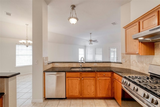 kitchen with stainless steel appliances, a healthy amount of sunlight, a sink, dark stone countertops, and under cabinet range hood