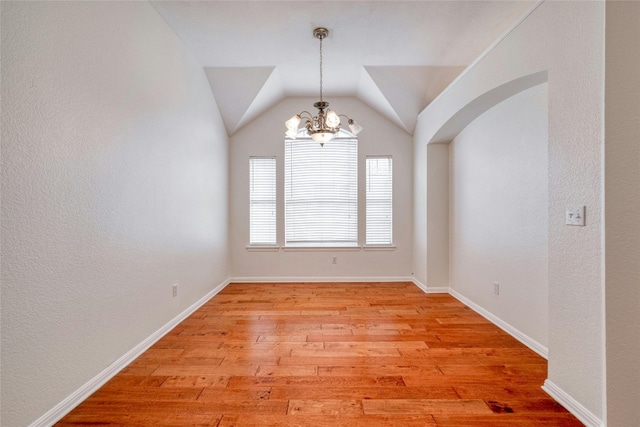 unfurnished room featuring arched walkways, a notable chandelier, baseboards, vaulted ceiling, and light wood finished floors