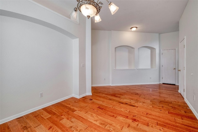 empty room featuring arched walkways, light wood-style flooring, and baseboards