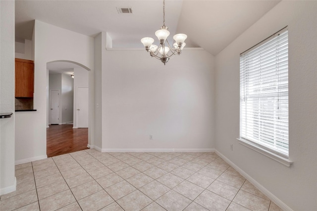 spare room featuring arched walkways, light tile patterned floors, visible vents, vaulted ceiling, and baseboards