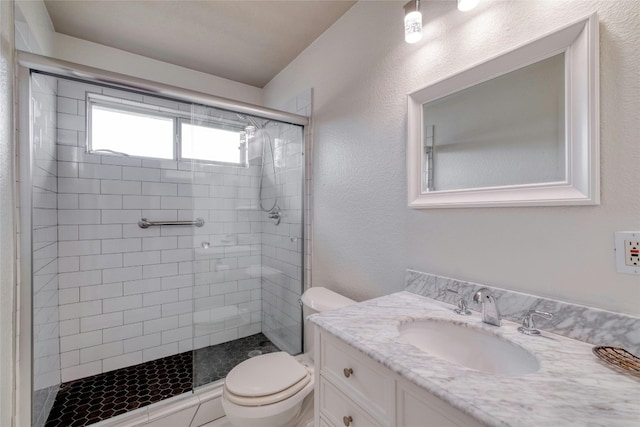 bathroom featuring a textured wall, a stall shower, vanity, and toilet