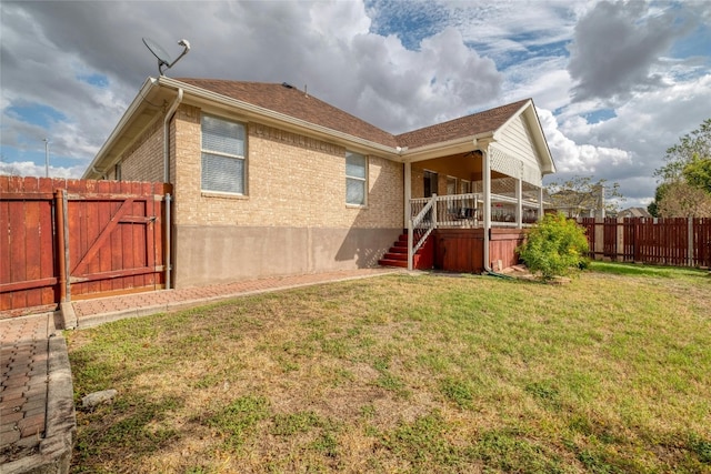 rear view of property with a yard, brick siding, fence, and a gate