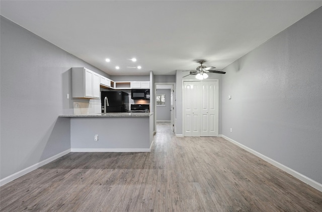 kitchen featuring kitchen peninsula, light stone countertops, light wood-type flooring, black appliances, and white cabinetry