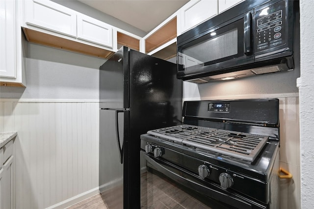 kitchen with black appliances, white cabinetry, and hardwood / wood-style flooring