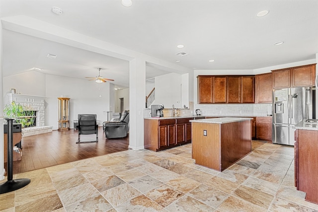 kitchen with decorative backsplash, light wood-type flooring, ceiling fan, stainless steel fridge with ice dispenser, and a center island