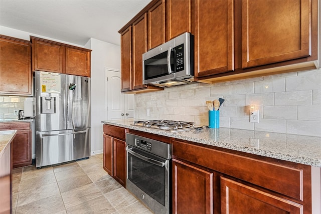 kitchen with light stone countertops, appliances with stainless steel finishes, and backsplash