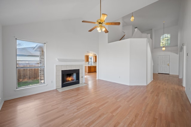 unfurnished living room with high vaulted ceiling, a tile fireplace, light hardwood / wood-style flooring, and ceiling fan