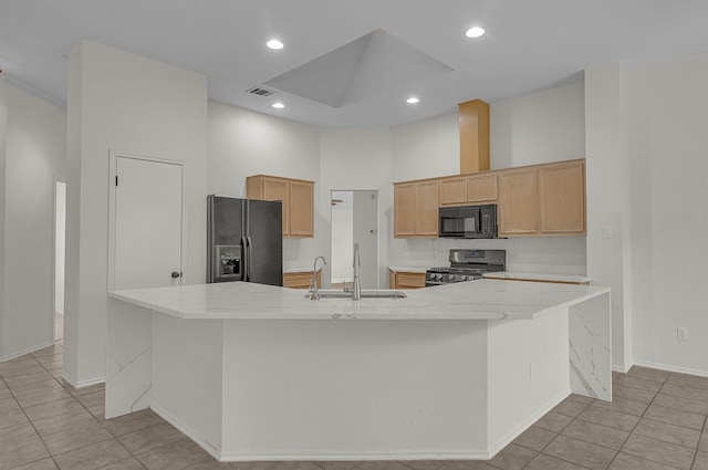 kitchen featuring light brown cabinetry, a center island with sink, and black appliances