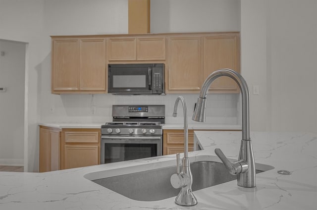 kitchen with tasteful backsplash, light stone counters, light brown cabinetry, and stainless steel gas range