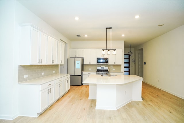 kitchen featuring stainless steel appliances, an island with sink, light hardwood / wood-style floors, decorative light fixtures, and white cabinets