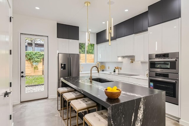 kitchen with a breakfast bar area, appliances with stainless steel finishes, backsplash, a center island with sink, and decorative light fixtures