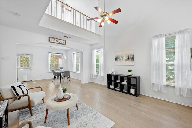 living room with ceiling fan, a high ceiling, and light hardwood / wood-style flooring