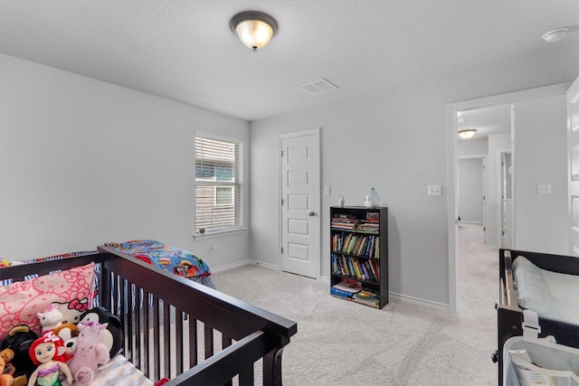 bedroom featuring a crib, a textured ceiling, and light colored carpet