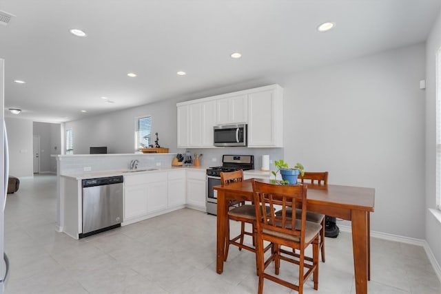 kitchen with sink, kitchen peninsula, light tile patterned floors, white cabinetry, and stainless steel appliances