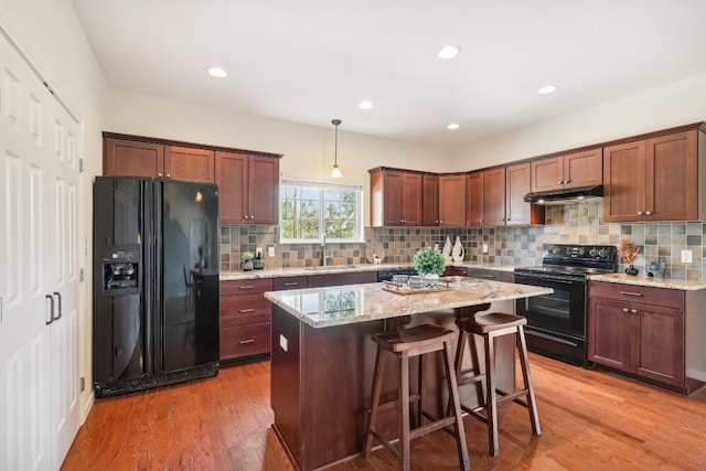 kitchen featuring wood-type flooring, light stone counters, a kitchen island, and black appliances