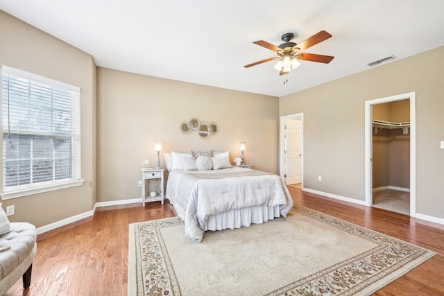 bedroom with a spacious closet, a closet, ceiling fan, and wood-type flooring