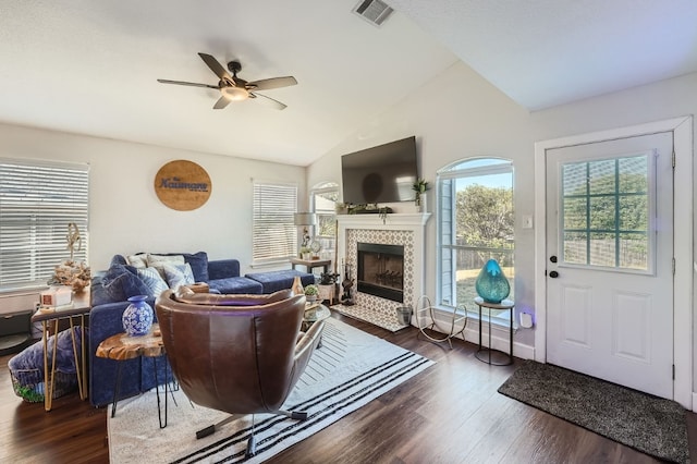 living room with dark hardwood / wood-style floors, vaulted ceiling, ceiling fan, and a tiled fireplace