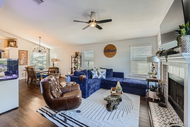 living room featuring dark hardwood / wood-style floors, a tiled fireplace, ceiling fan with notable chandelier, and vaulted ceiling