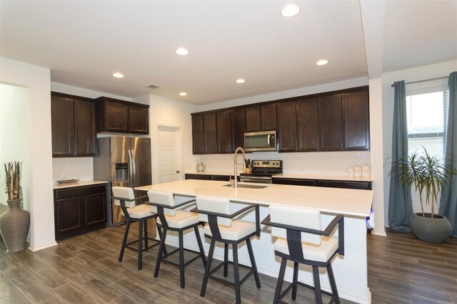 kitchen with dark hardwood / wood-style floors, sink, appliances with stainless steel finishes, and an island with sink