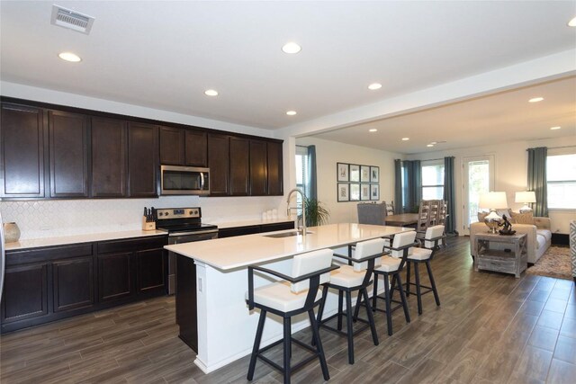 kitchen with stainless steel appliances, sink, a center island with sink, dark hardwood / wood-style floors, and a breakfast bar area